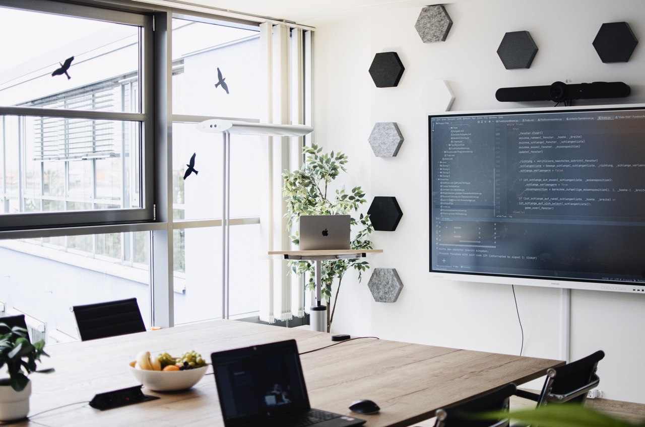 Schulungsraum von SimplyTest mit langem Tisch, Laptops und einem großen Bildschirm mit Programmcode