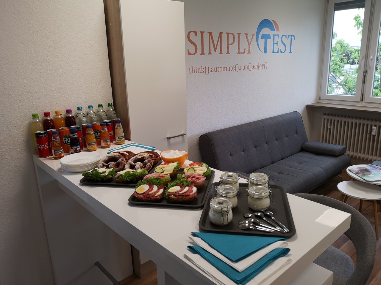 Büroküche mit gedecktem Buffet und Getränken, an der Wand das Logo von SimplyTest