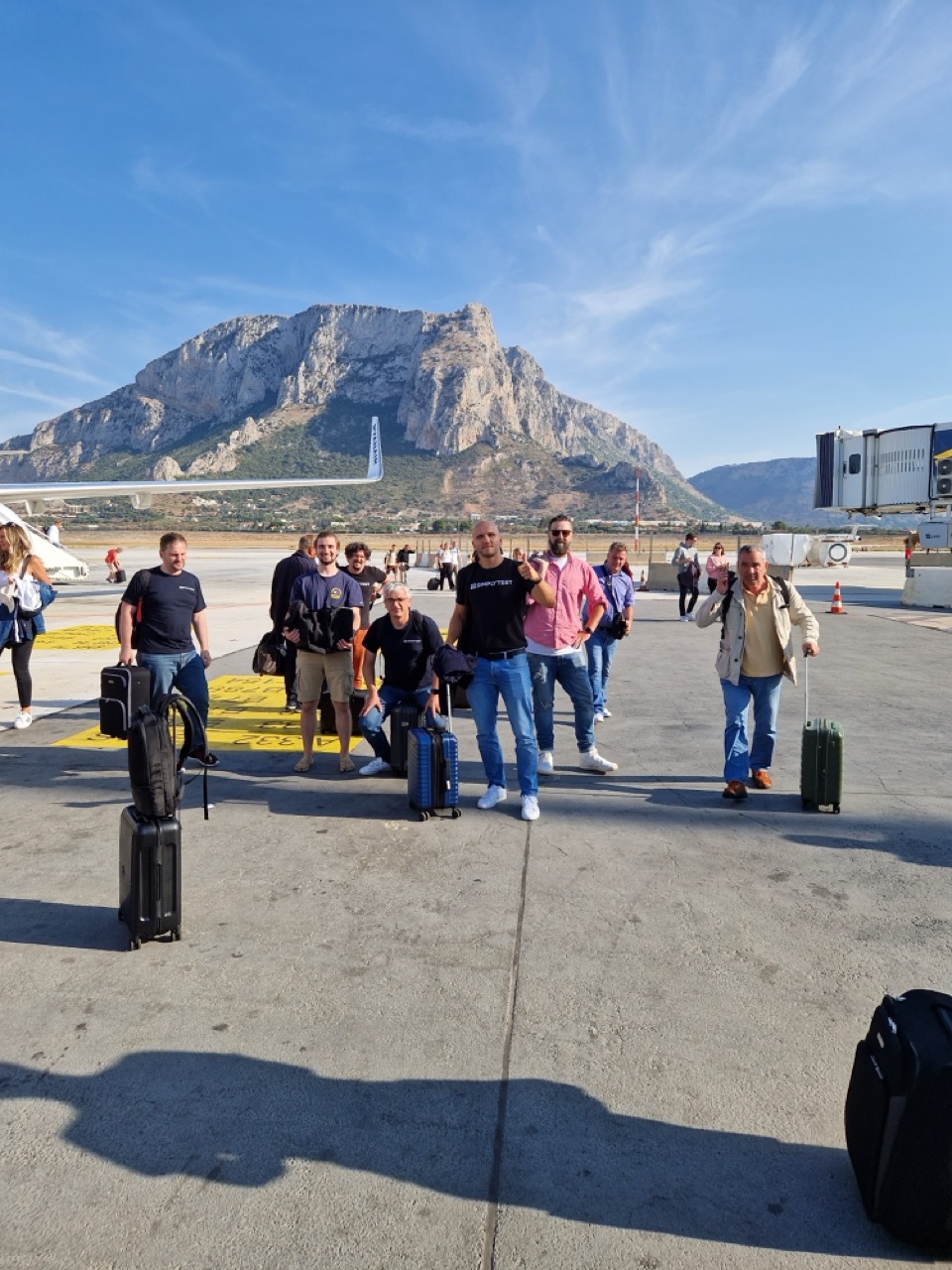 Das Team kommt mit Koffern am Flughafen an, im Hintergrund ein Berg
